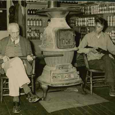 Louis P. Cole and Carl Bryant cleaning their guns next to the stove in Cole's Store.