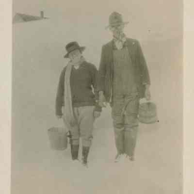 Two people walking in the snow carrying buckets