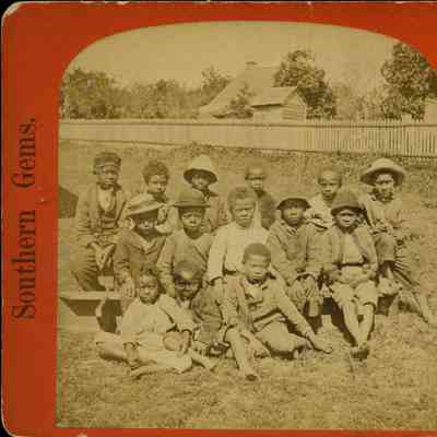 Group of Black children sitting on grass in front of fence and house