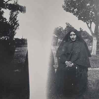 Religious family member of the Retaliate family in dark traditional attire is sitting outdoors.