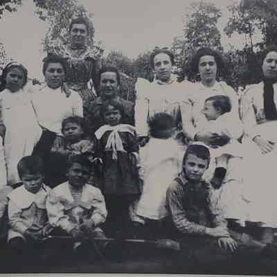 The black-and-white photo shows a group of people, mainly women and children.