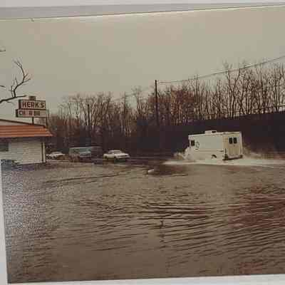 White van driving through flooded street past Herks Char Broil