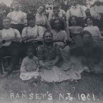 A group of people pose together outdoors, some seated and others standing, with one playing guitar.