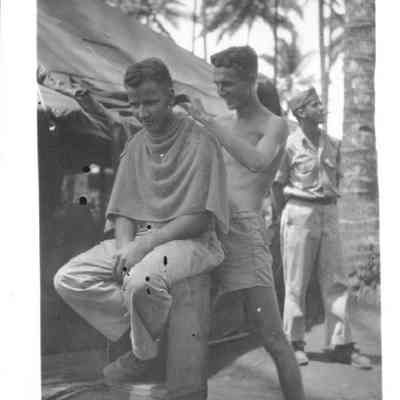 Photo of two men, one cutting the other person's hair during WWII.