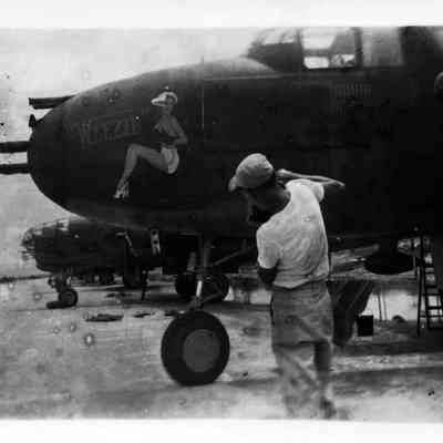 Man taking picture of name and woman's picture on WWII plane.