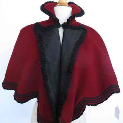 Red wool capelet with black ruffled trim, ribbon trim and stand up collar