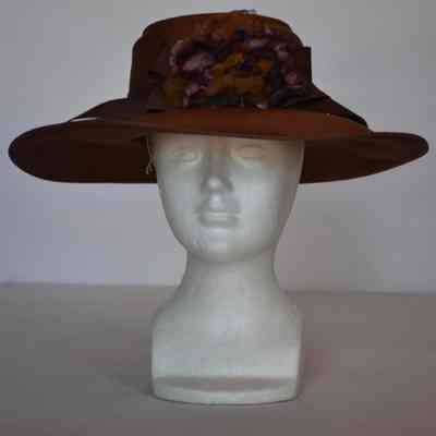 Wide brim woven hat with chocolate colored grograin ribbon and purple flower detail.