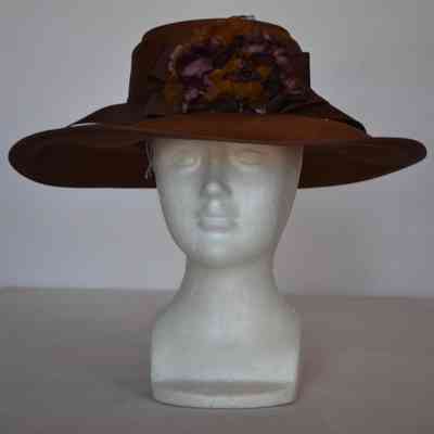 Wide brim woven hat with chocolate colored grograin ribbon and purple flower detail.