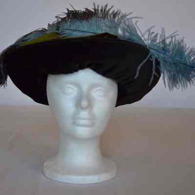 Black velvet brimmed pancake style with large blue feather and green crown
