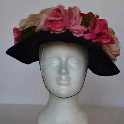 Black velvet brimmed hat with large pink and cream flowers around front brim