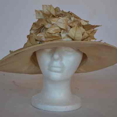 Fabric covered hat with wider brim at front, shorter brim at back with decorative leaves covering front crown