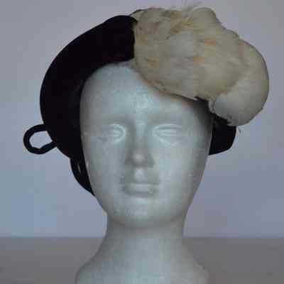 Velvet casque with narrow brim and white feather embellishment on left front, velvet cording bow