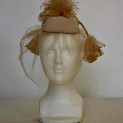 Small pillbox with net pouf on crown, front veil and pom poms attached with long velvet cords