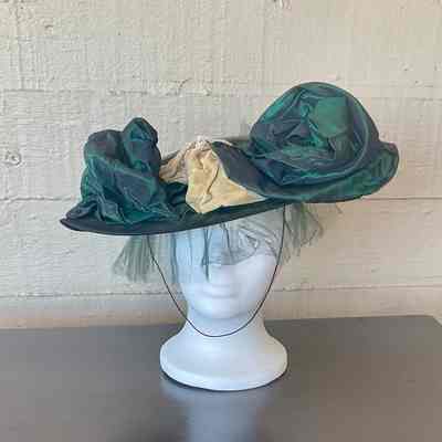 Black fabric platter hat with green/black iridescent fabric accents, green tulle and cream velvet ribbon