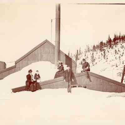 Photo 2: Two women, two men, and a child on the roof of a building where snow comes up to the top of the window. Written in pencil on back of photo: "Apex, Colo, 1899, 9500 ft high"