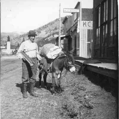 2. Man and burro: A man and his pack burro in front of the boardwalk and several stores, including a Meat Market, in Eldora, identified as Bob (?), 1907 (?), Eldora Colo.