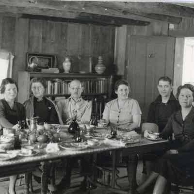7. Inside the Kemp cabin, Lois Kemp is third from left, other people unknown: Six people sit around table after dinner.