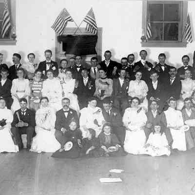 Men, women and children in hall with flags, c. 1915.