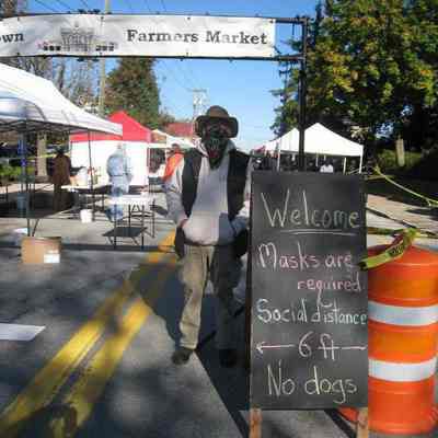 Mask wearer at entrance sign to Charles Town Farmers Market