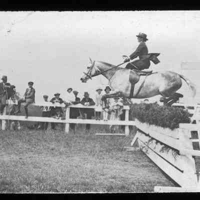 Woman jumping a horse at a horse show while riding side-saddle