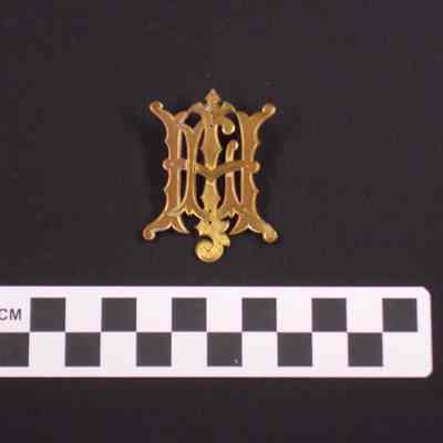 Thin, flat, gold-colored metal brooch in the shape of initials or monogram