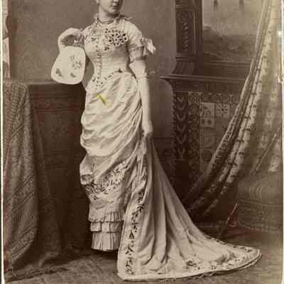 Young woman in elaborate dress with train, long gloves, and fan