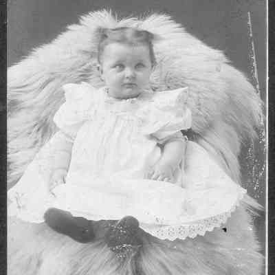 Child in white dress sitting on animal skin rug