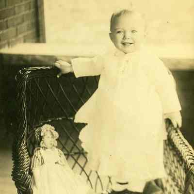 Catherine Rutherford Packette standing in a wicker chair with a doll