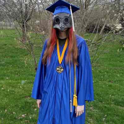 Sophia Smith in high school graduation robe with plague doctor mask (IMG3782002)