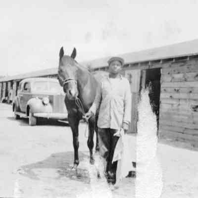 Unidentified race track stables, horse, and worker