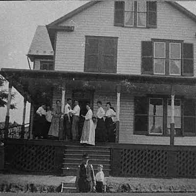 Merchant family and unidentified young women standing on porch of house (IMG3900002)