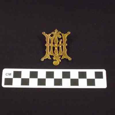 Thin, flat, gold-colored metal brooch in the shape of initials or monogram