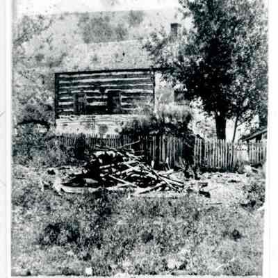 Photograph of exterior of the farmhouse showing wooden fence and pile of lo