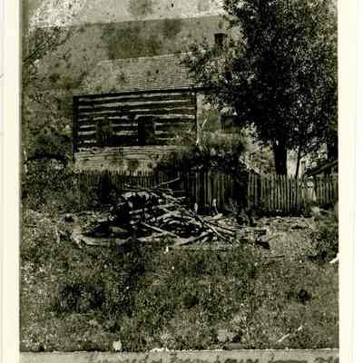Photograph of exterior of farmhouse showing wooden fence and pile of logs