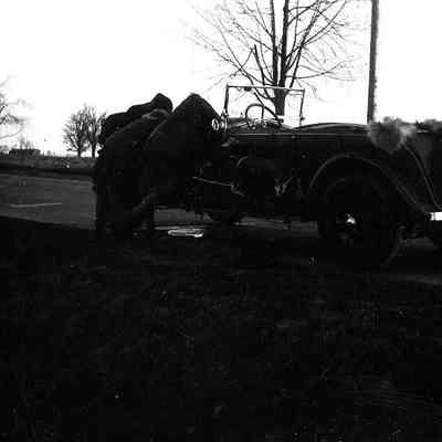2021.12.310b: Very dark photo of two people leaning into a car outdoors.