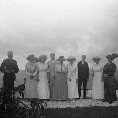 2021.12.310e: Nine people stand outdoors in formal attire, facing the camera, with a scenic background.