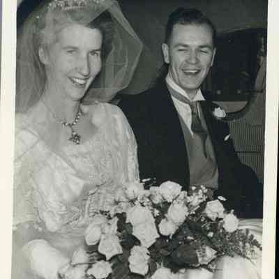 Photo - 2021.12.289j: A joyful Dorothy and Harold Burnham laugh together in a car, while Dorothy hold a bouquet of white roses.