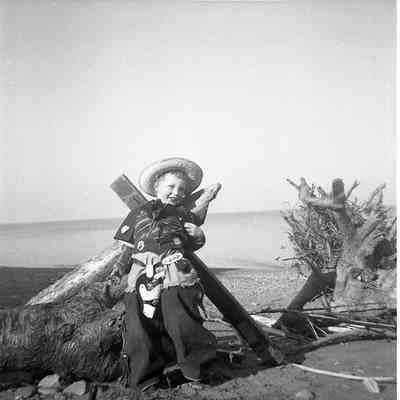 2021.12.309d: A child dressed as a cowboy poses on a beach.