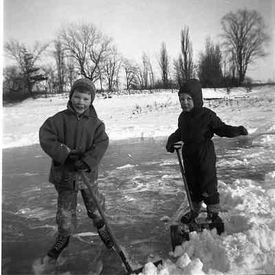 2021.12.309m: Two boys, Mark and James Burnham, are clearing snow on a frozen pond, dressed warmly in winter clothing.