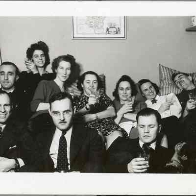 2021.12.297c: Identical copy of 2021.12.297b. A group of ten adults enjoys a lively gathering, holding drinks and smiling in a cozy room. Dorothy Burnham is the 3rd from the left in the back row, Harold Burnham is in the front row, farthest to the right (looking down towards glass). All other names unknown.
