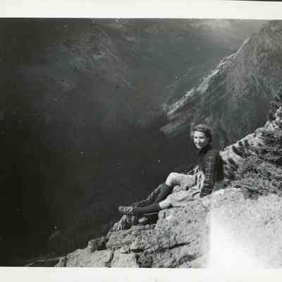 Photograph of Dorothy - 2021.12.291e: Dorothy sitting on the rocks at Sunshine Valley - The Simpson Pass. There is black construction paper attached to this photo and cut to fit the dimensions of the photo.