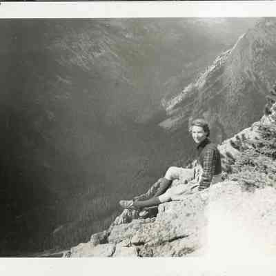 Photograph of Dorothy - 2021.12.291f: The same photograph (2021.12.291e) of Dorothy sitting on the rocks at Sunshine Valley - The Simpson Pass. Photo is attached to black construction paper with two holes punched in it. (Likely part of a scrapbook at one point)