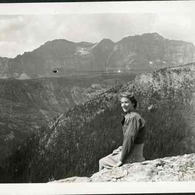 Photograph of Dorothy - 2021.12.291i: Dorothy sitting on the rocks at Sunshine Valley - The Simpson Pass. Photo is attached to black construction paper with two holes punched in it. (Likely part of a scrapbook at one point).