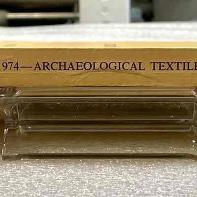 1974 Proceedings: Archaeological Textiles - Side View: Spine of book, yellow card cover with black lettering.