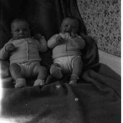 2021.12.311k: The image shows the twins, James and Harold Burnham sitting closely together on a draped fabric.