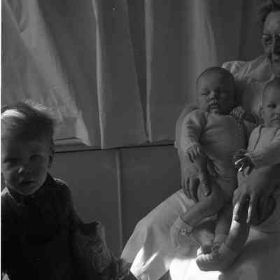 2021.12.311n: A woman sit holding the twins, James and Harold Burnham, while Mark Burnham sits in front of them.