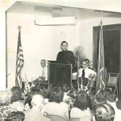 Male speaker, unidentified, at a podium speaking to a group of seated persons