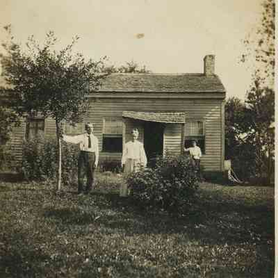 Unidentified Man and Woman and third Person in front of an old Farm House