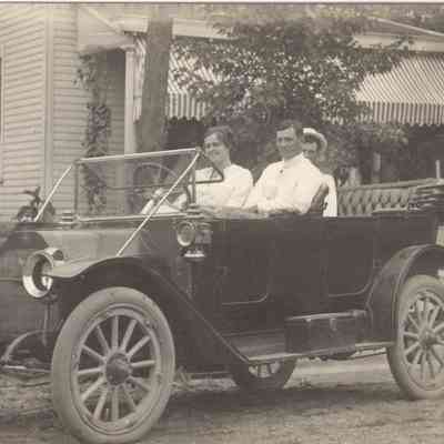 Actual Photo Post Card of three people sitting in and old car wearing white clothes