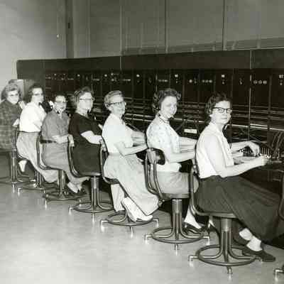Seven seated women, unidentified, at switchboard consoles